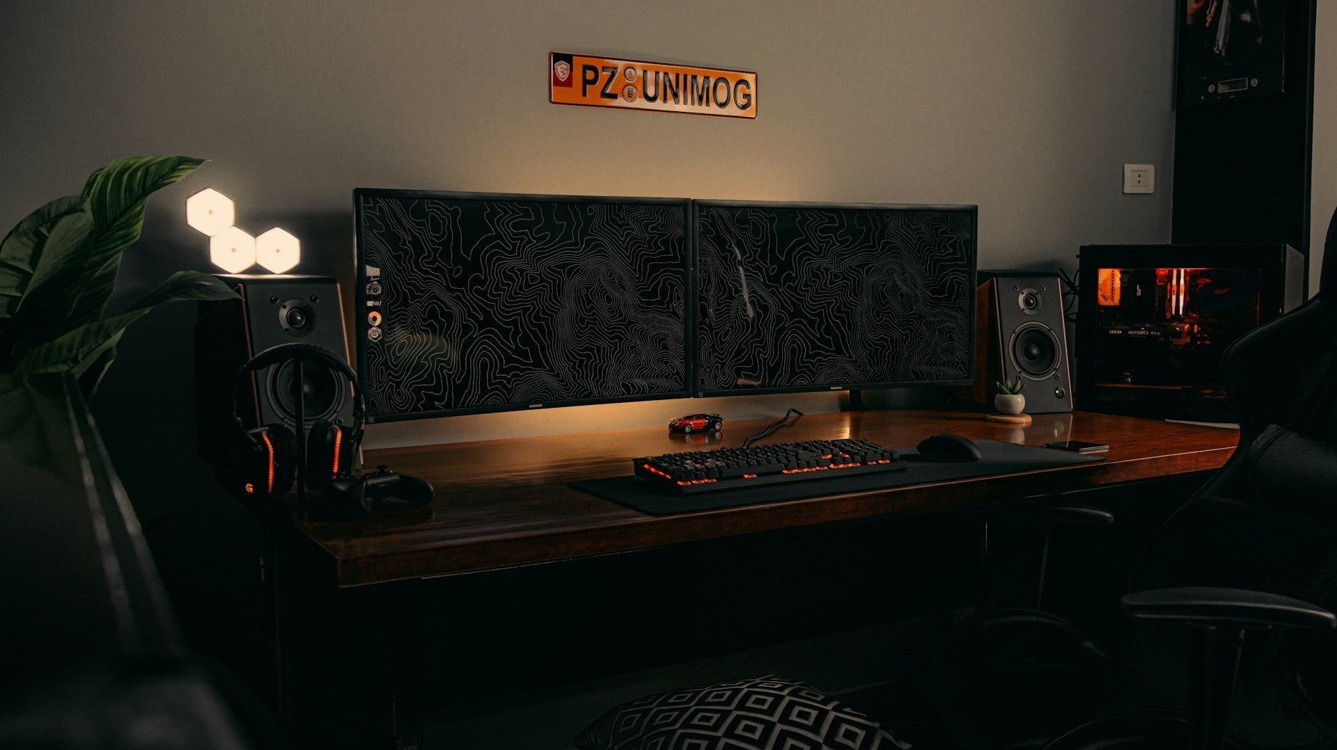 Modern corner gaming desk setup with dual monitors, speakers, gaming keyboard, and ambient lighting in a stylish home office