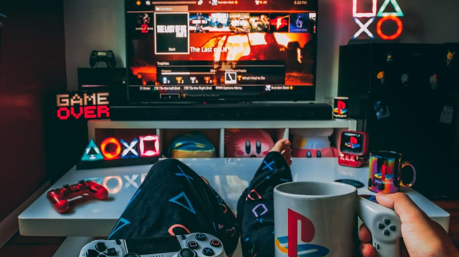 Gamer holding PlayStation mug and controller in a stylish setup showcasing gaming room essentials like decor and lighting. Photo by Branden Skeli via Unsplash