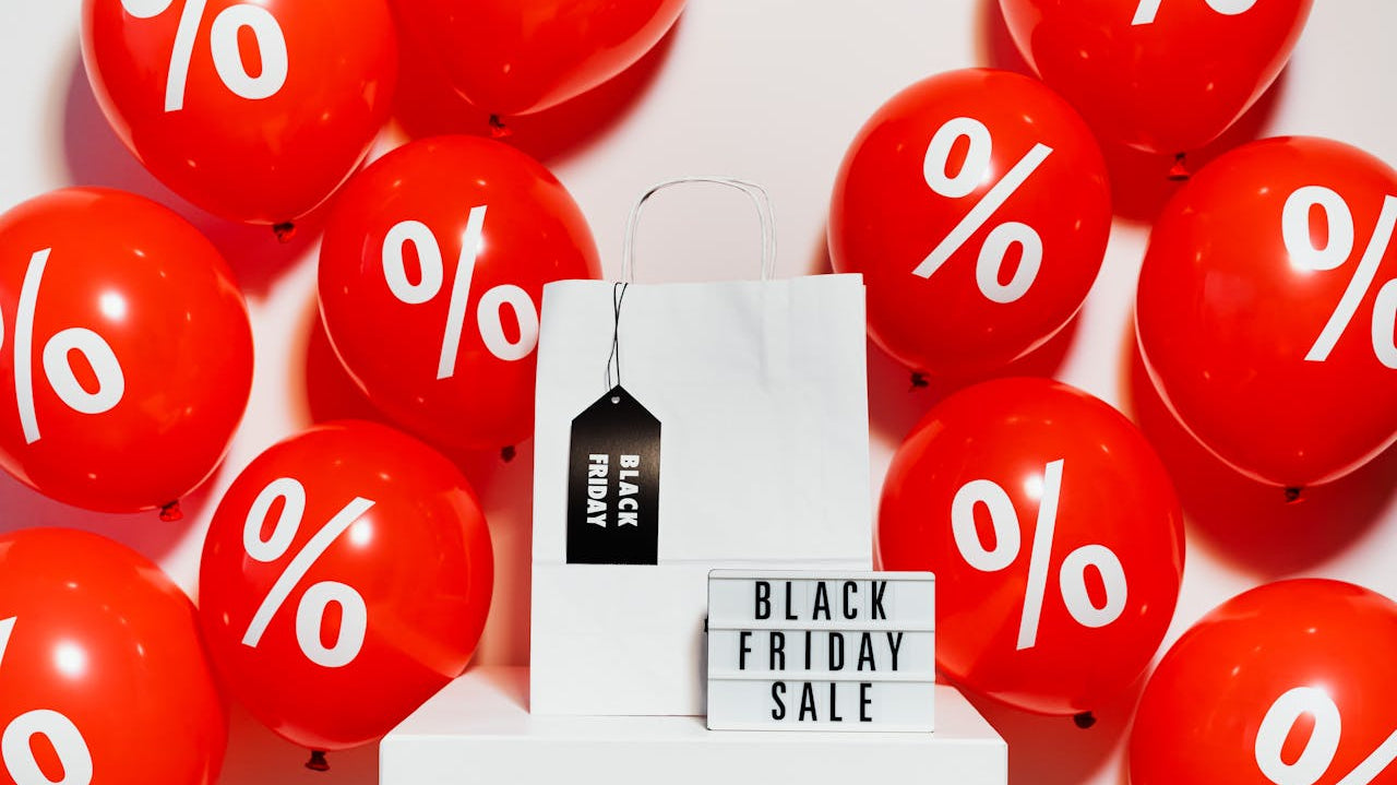 Red and White Balloons on White Wall, a white shopping bag, and a black friday sale signage. Image by Karola G via www.pexels.com