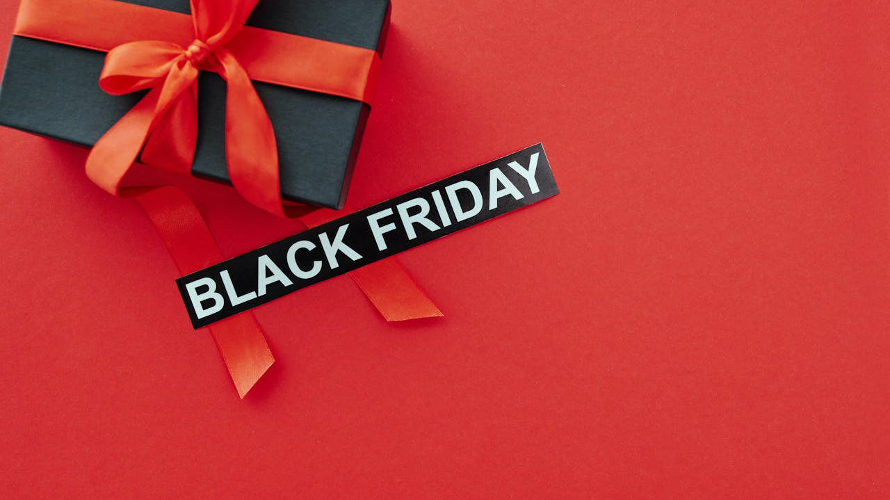 a black gift box with a red ribbon and a sign that says black on a red platform. Image by Max Fischer via. www. pexels.com