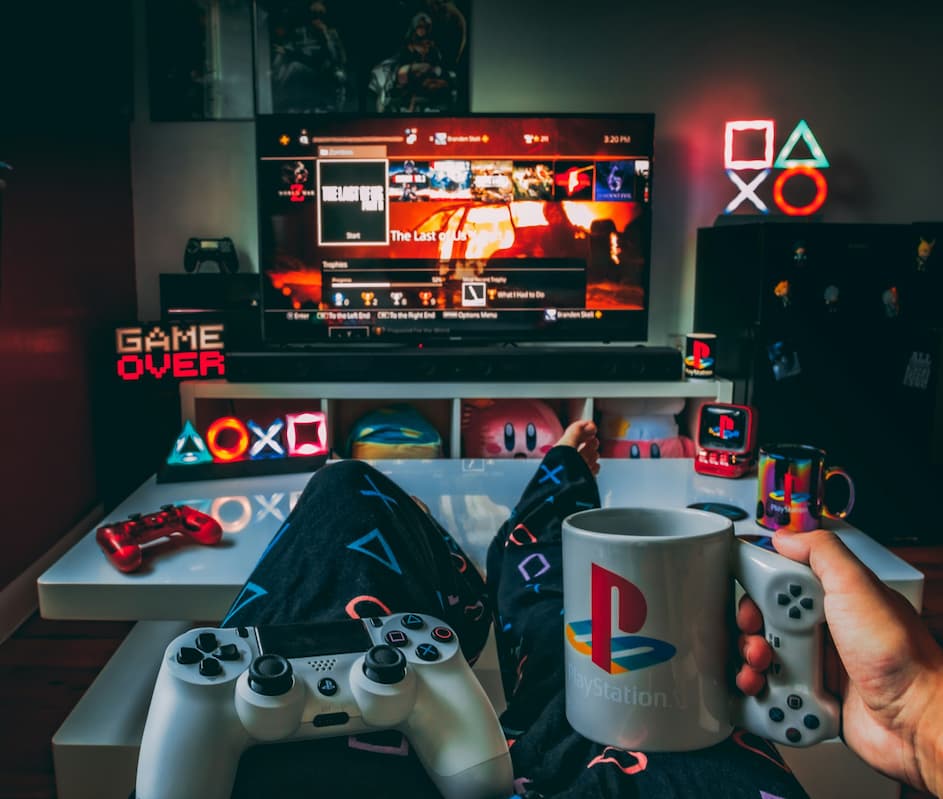 Gamer holding PlayStation mug and controller in a stylish setup showcasing gaming room essentials like decor and lighting. Photo by Branden Skeli via Unsplash