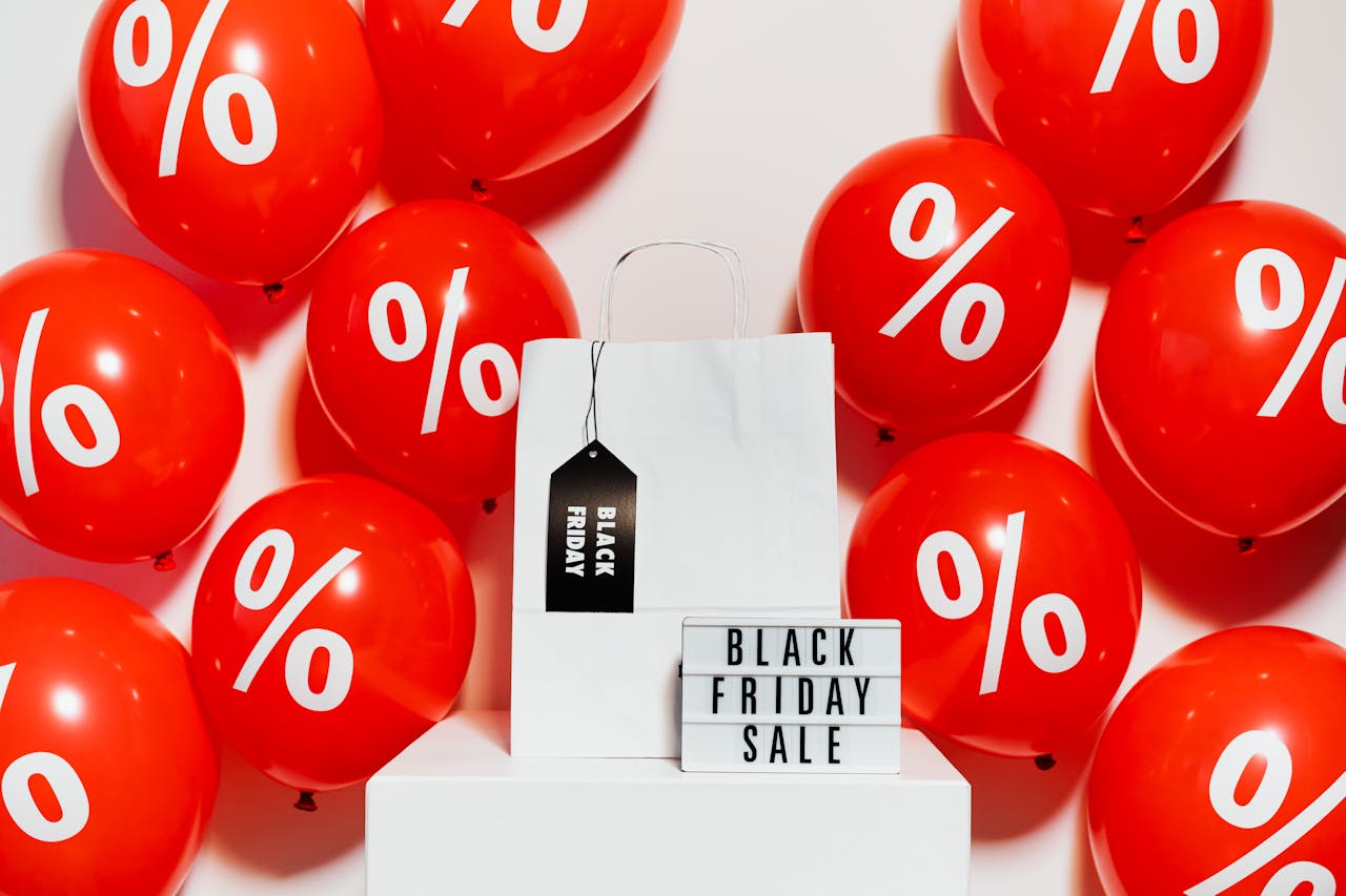 Red and White Balloons on White Wall, a white shopping bag, and a black friday sale signage. Image by Karola G via www.pexels.com