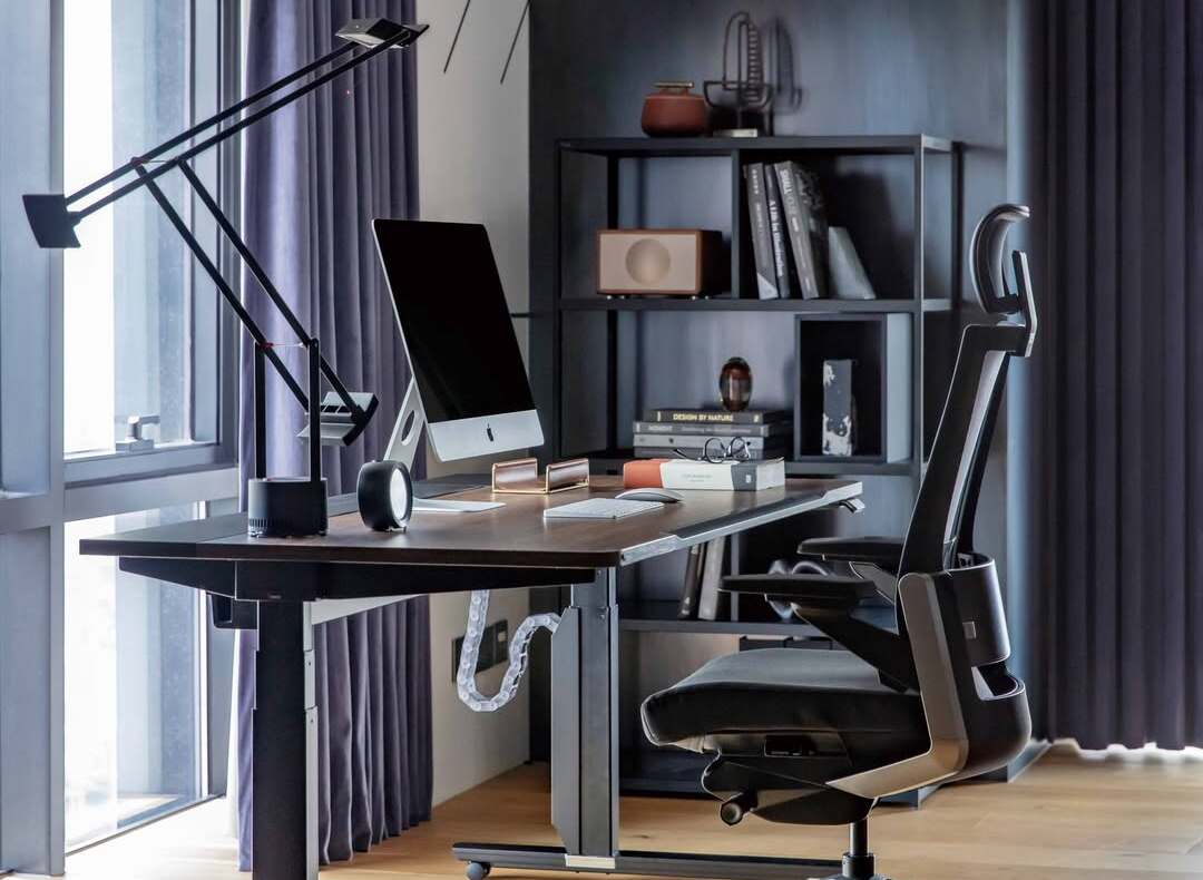 Modern home office setup featuring an ergonomic chair, standing desk, monitor, and organised cable management by a large window