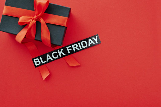 a black gift box with a red ribbon and a sign that says black on a red platform. Image by Max Fischer via. www. pexels.com