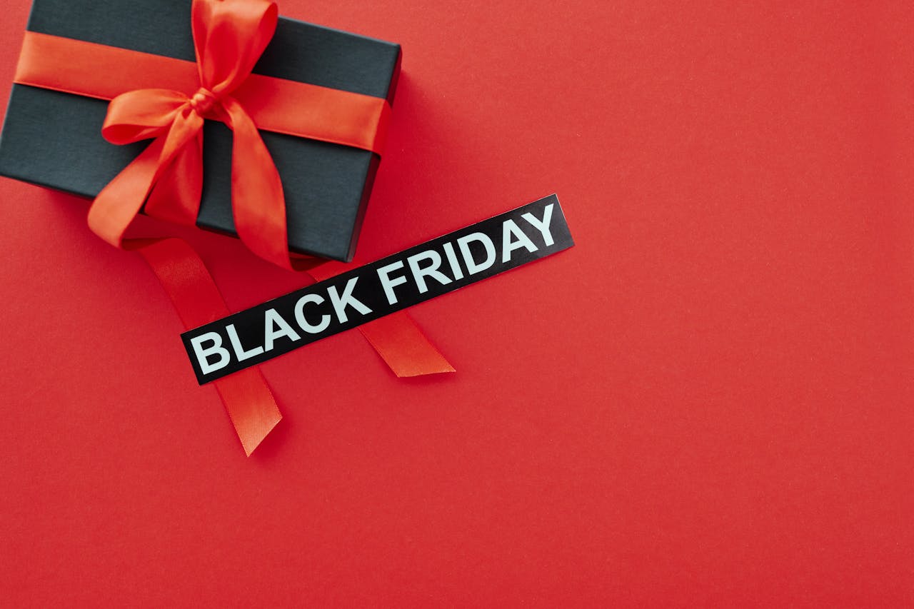 a black gift box with a red ribbon and a sign that says black on a red platform. Image by Max Fischer via. www. pexels.com